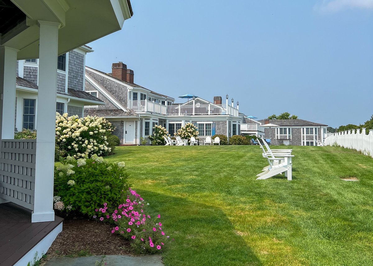 A charming Cape Cod coastal home with gray shingles, vibrant flowers, and Adirondack chairs on a lush green lawn