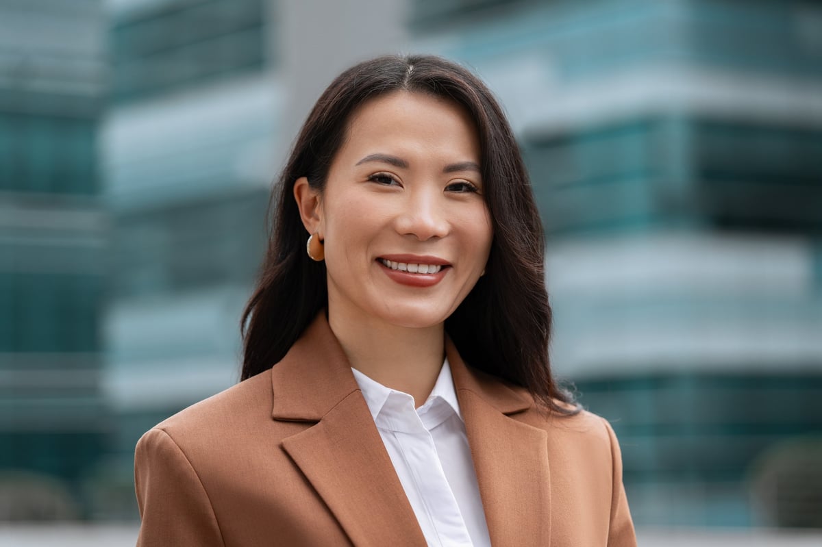 Smiling mature Asian successful businesswoman standing outdoors, looking at camera at skyscrapers office building. Close-up portrait of middle-aged beautiful woman, business leader entrepreneur